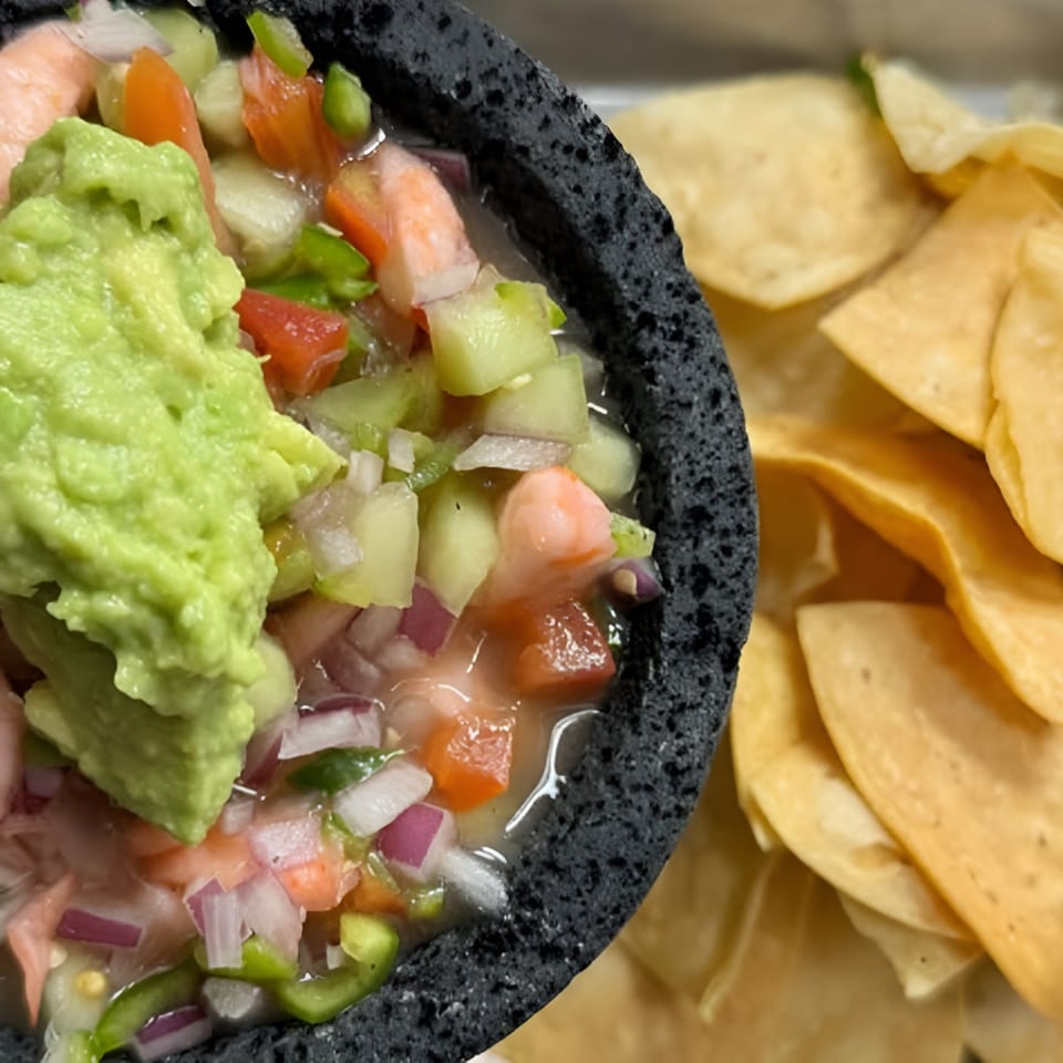 Shrimp ceviche with guacamole in a dark bowl, served with a side of tortilla chips.