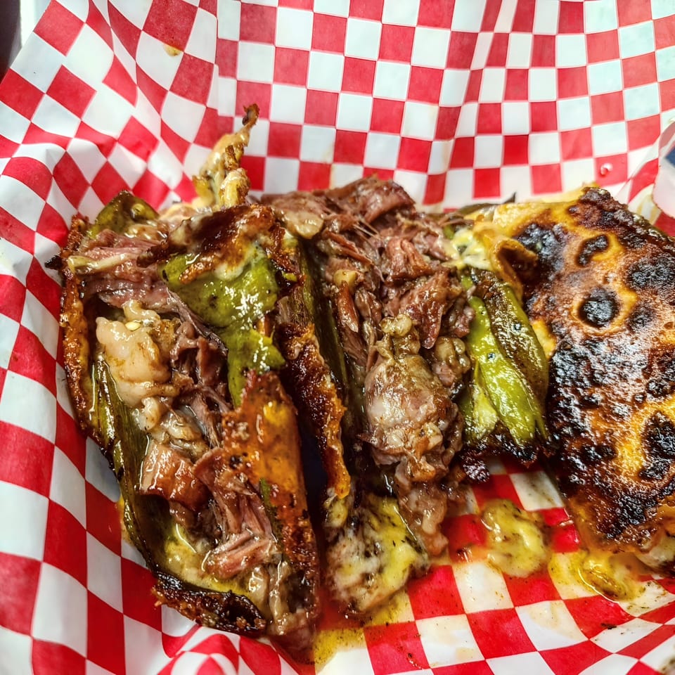 The Taco Man's Mexican dish with charred peppers, melted cheese, and shredded meat in a red and white checkered basket.