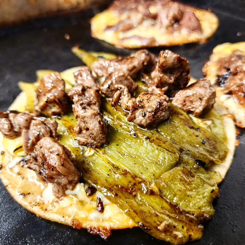 Close-up of a sizzling taco with grilled meat and green peppers on a griddle.