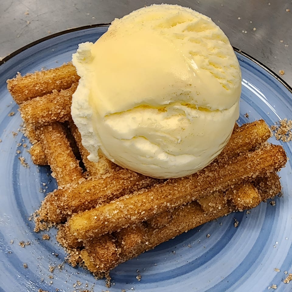 Churros with cinnamon sugar and a scoop of vanilla ice cream on a blue plate.